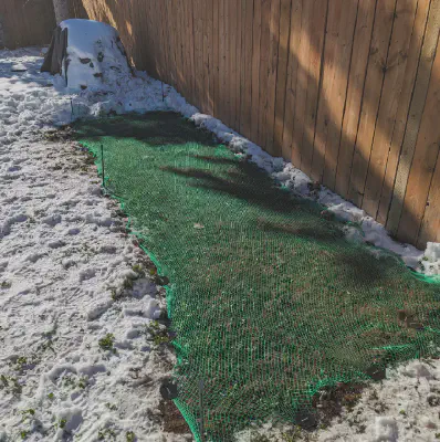 Green netting covers a rectangular shaped garden, surrounded by snow.